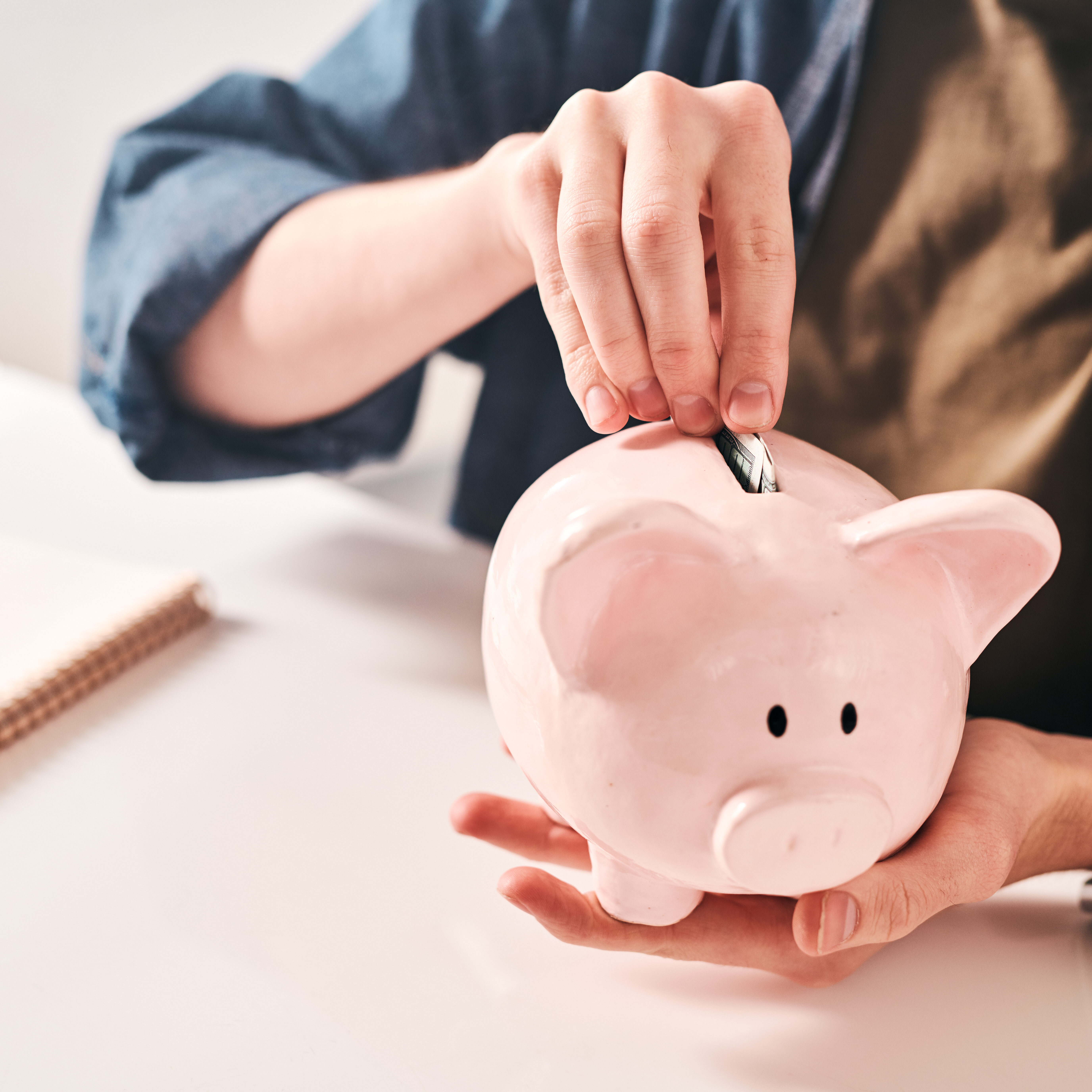 Close-up of unrecognizable man sitting at table and putting coins into piggybank while saving money in crisis